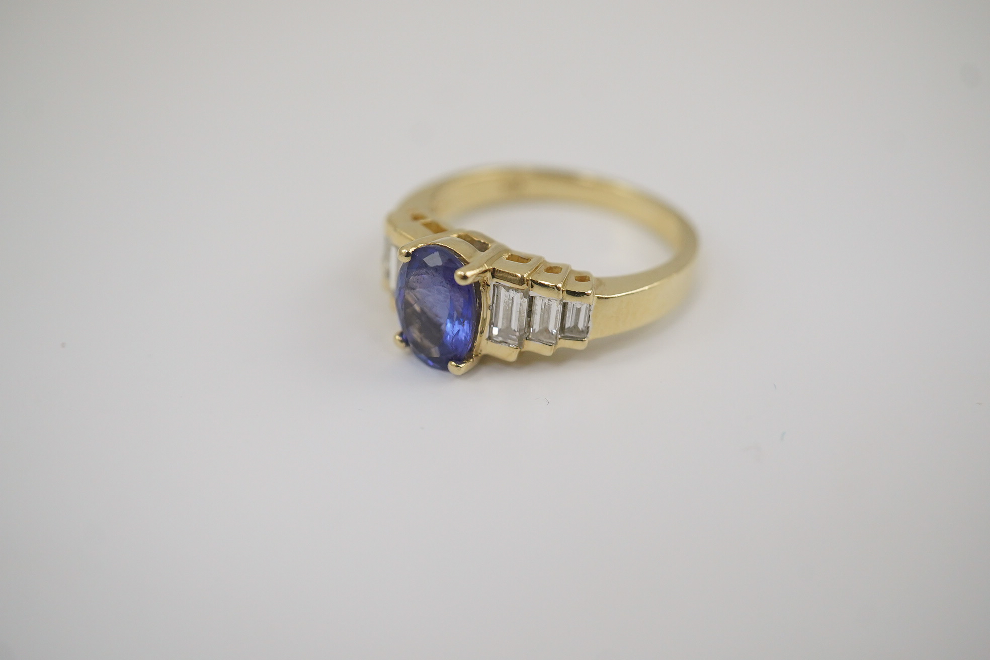 A modern 14k gold and single stone oval cut tanzanite set dress ring, with six stone graduated baguette cut diamond set shoulders